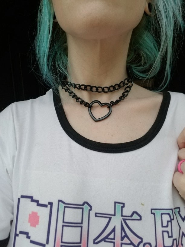 Black double-chain heart choker styled with a white graphic T-shirt with black neck trim, photographed on a wearer with blue-green hair.