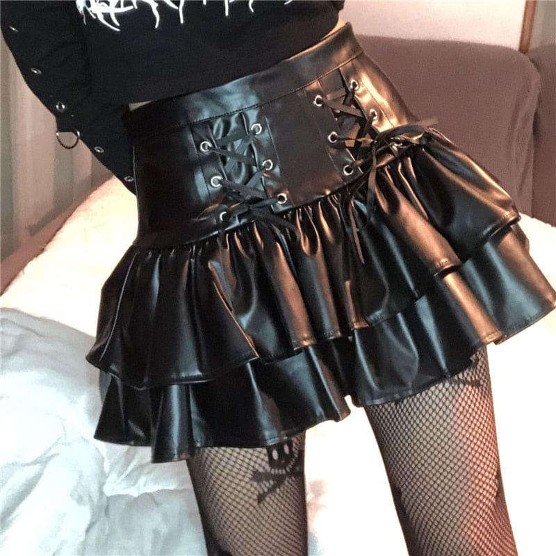Another angled view of the black faux leather skirt under warm light, highlighting the paired lacing panels and folded ruffle edges.