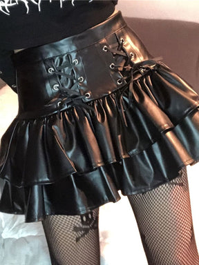 Angled close view of a glossy black ruffle skirt styled with fishnet stockings, showing ribbon lacing across the high waist and the layered short hem.