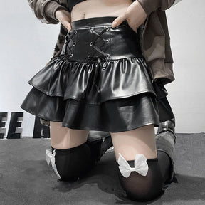 Closer kneeling outfit view of the glossy black ruffle skirt with a dark coat and bow-trimmed stockings, keeping the front lacing in view.