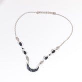 Silver-tone headdress with a black marbled acrylic crescent and large black teardrop beads, arranged in an oval on a pale background with the clasp and chain visible.