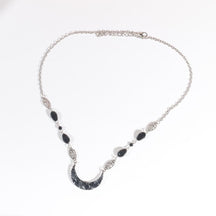 Silver-tone headdress with a black marbled acrylic crescent and large black teardrop beads, arranged in an oval on a pale background with the clasp and chain visible.