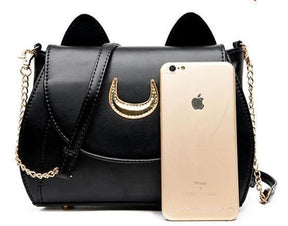 Black cat-ear moon bag beside a gold-coloured phone for visual comparison, with its chain and strap draped across the front.