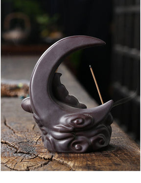 Back of the dark Black moon burner on weathered wood, showing its smooth crescent curve and rounded scroll details at the base.