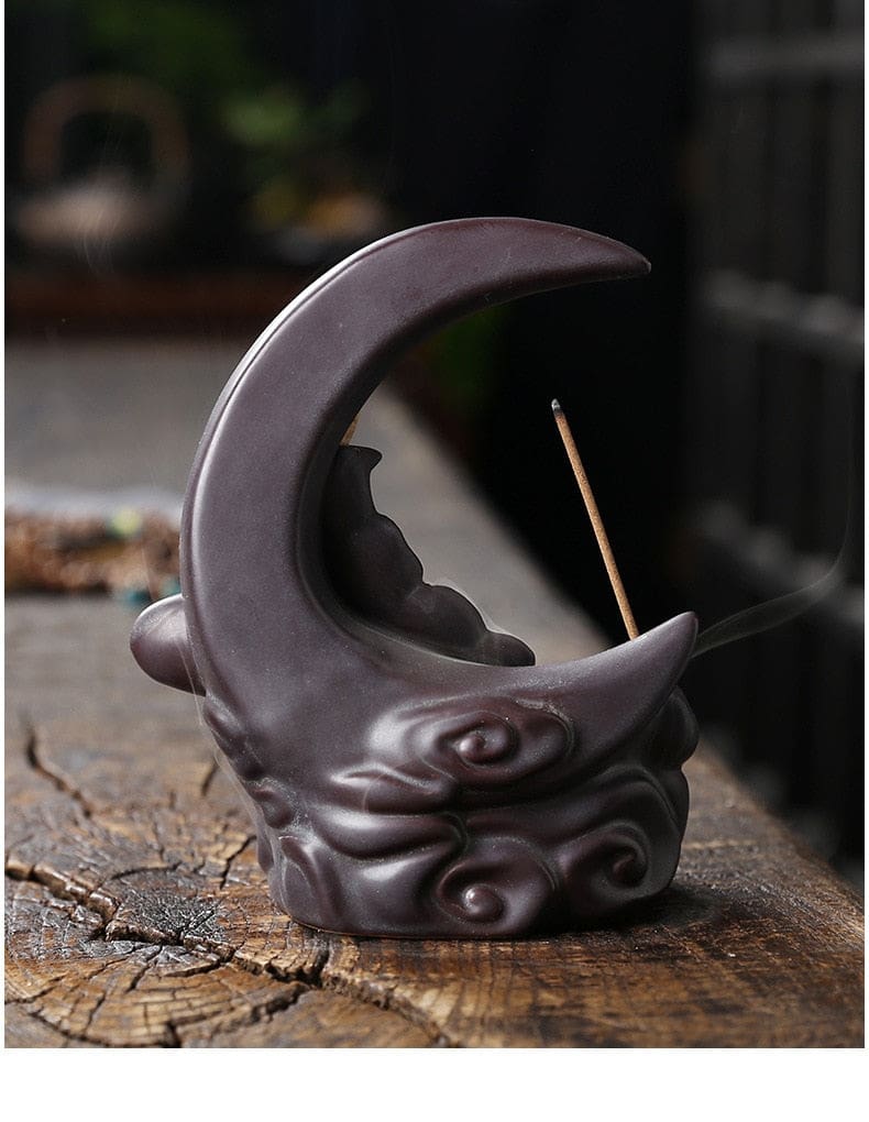 Back of the dark Black moon burner on weathered wood, showing its smooth crescent curve and rounded scroll details at the base.