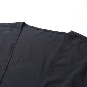 Close-up of the plain neckline seam and front edge of the black draped shawl.
