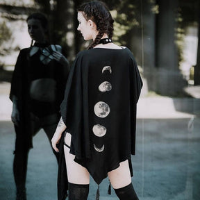 Black celestial wrap worn outdoors, with pointed sides and tassels visible below the lunar print.