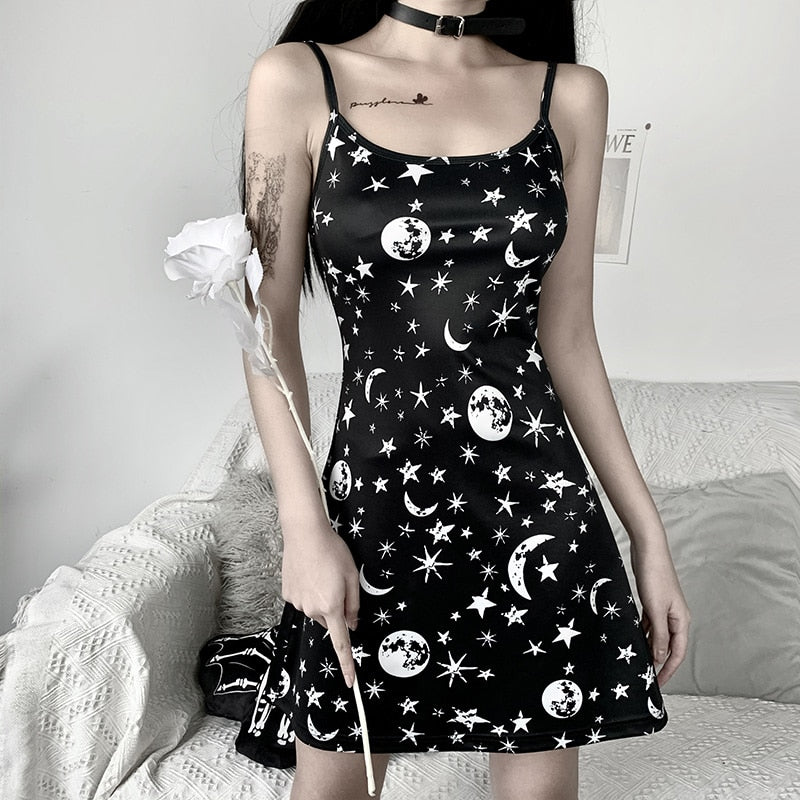 Black moon and star print mini dress shown from the front beside a white flower prop.
