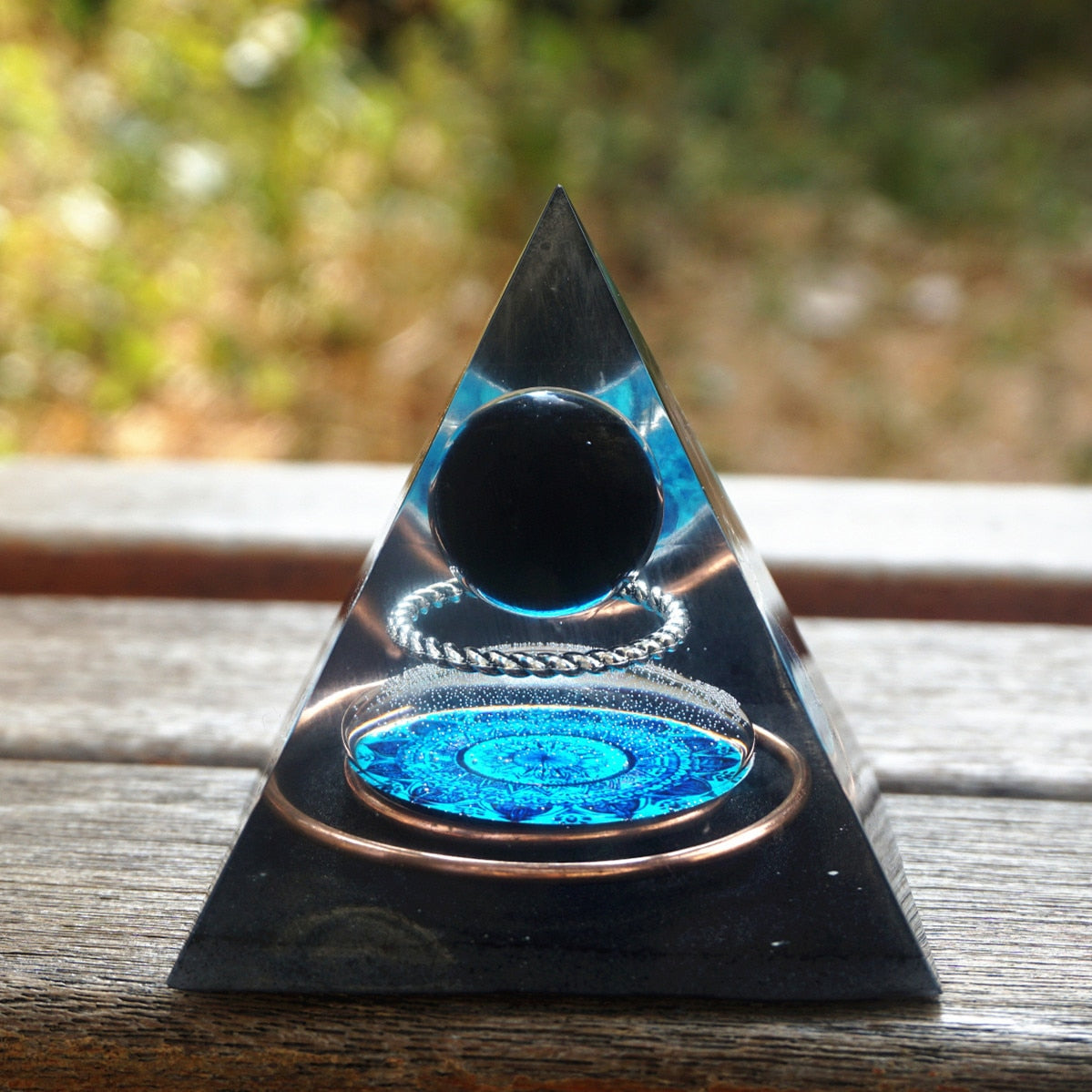 Additional view of Black obsidian orgone pyramid with a dark sphere, blue mandala and copper loops. The wood display composition again shows the nested circular details.