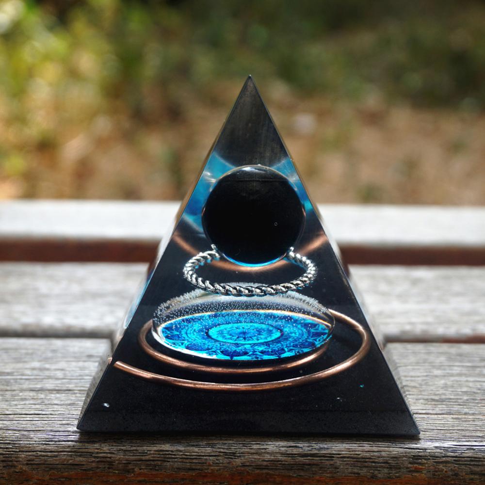 Black obsidian orgone pyramid with a dark sphere, blue mandala and copper loops. Standing on wood with copper loops surrounding the central mandala.