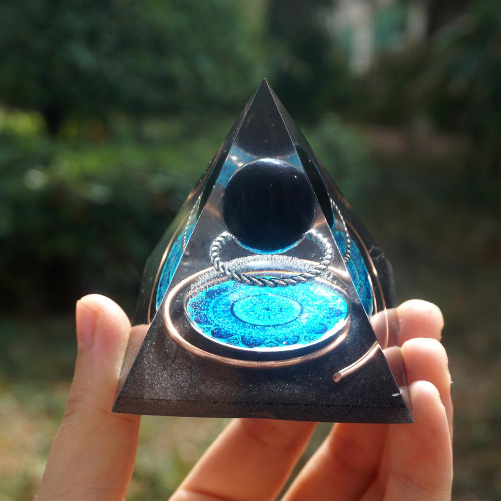 Additional view of Black obsidian orgone pyramid with a dark sphere, blue mandala and copper loops. A repeated full view shows the pyramid held against a leafy background.