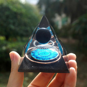 Black obsidian orgone pyramid with a dark sphere, blue mandala and copper loops. Held farther from the camera to show the complete pointed outline.