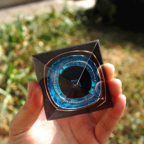 Black obsidian orgone pyramid with a dark sphere, blue mandala and copper loops. Top view showing the square footprint, black sphere and blue circular inlay.