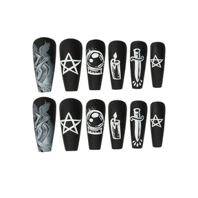 Black coffin-shaped press-on nails arranged on white, with pale pentagrams, a candle, crystal ball, crescent, snake and dagger among smoky decorative details.