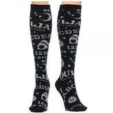 Black knee-high Ouija socks worn on crossed legs, showing white spirit-board lettering and celestial motifs around the calves.