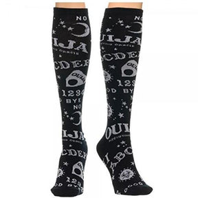 Black knee-high Ouija socks worn on crossed legs, showing white spirit-board lettering and celestial motifs around the calves.