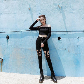 Full-length front view of black skinny pants with star-shaped straps across the thighs and an O-ring front zip, styled with black boots.