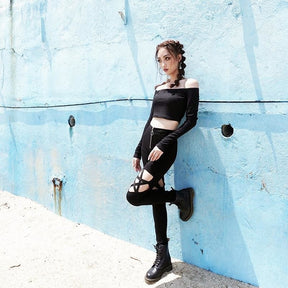 Black pentagram cutout pants styled with a cropped long-sleeve top and lace-up boots, shown with one leg bent against a blue wall.