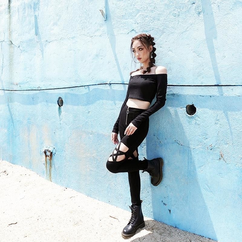 Black pentagram cutout pants styled with a cropped long-sleeve top and lace-up boots, shown with one leg bent against a blue wall.