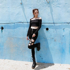 Angled standing view of the black pentagram pants, with open thigh panels visible beneath a cropped off-shoulder top.