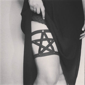 Black elastic leg garter with crossing straps forming a pentagram and round metal accents.