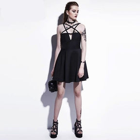 Full front outfit view of the black harness neckline skater dress with separate strappy heels and a small black bag against a pale studio wall.