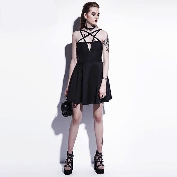 Full front outfit view of the black harness neckline skater dress with separate strappy heels and a small black bag against a pale studio wall.