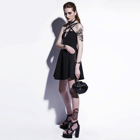 Angled full-length studio view of the black pentagram dress worn with separate heels and a small bag, with the flared hem casting a shadow on the pale wall.