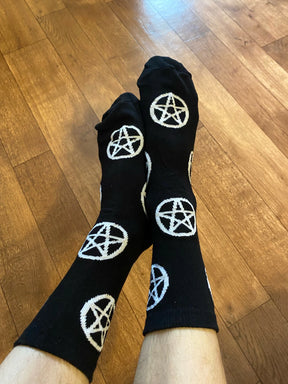 Black socks covered in white pentagrams worn with the feet crossed above a wooden floor, showing the repeating pattern down both legs.