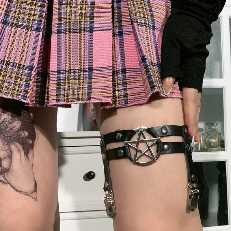 Close front view of the pentagram garter as a hand lifts the skirt hem, exposing the silver-tone star ring and parallel black straps.