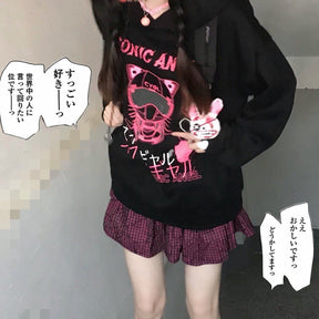 Front view of the black hoodie with pink graphic lettering and white hearts; comic-style text surrounds the model.