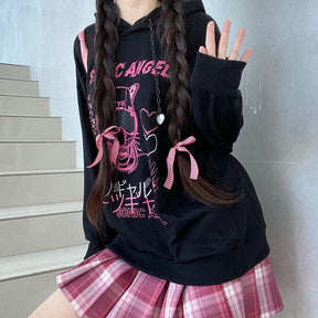 Front view of the black graphic hoodie showing its dropped shoulders and ribbed cuffs, with a pink shoulder bag.
