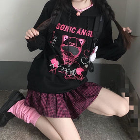 Wider seated outfit view of the black hoodie, pink plaid skirt and ribbed sleeve cuffs.