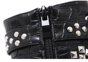 Close-up of the side zipper on a black reptile-textured ankle boot, bordered by straps with round and pyramid-shaped silver-tone studs.