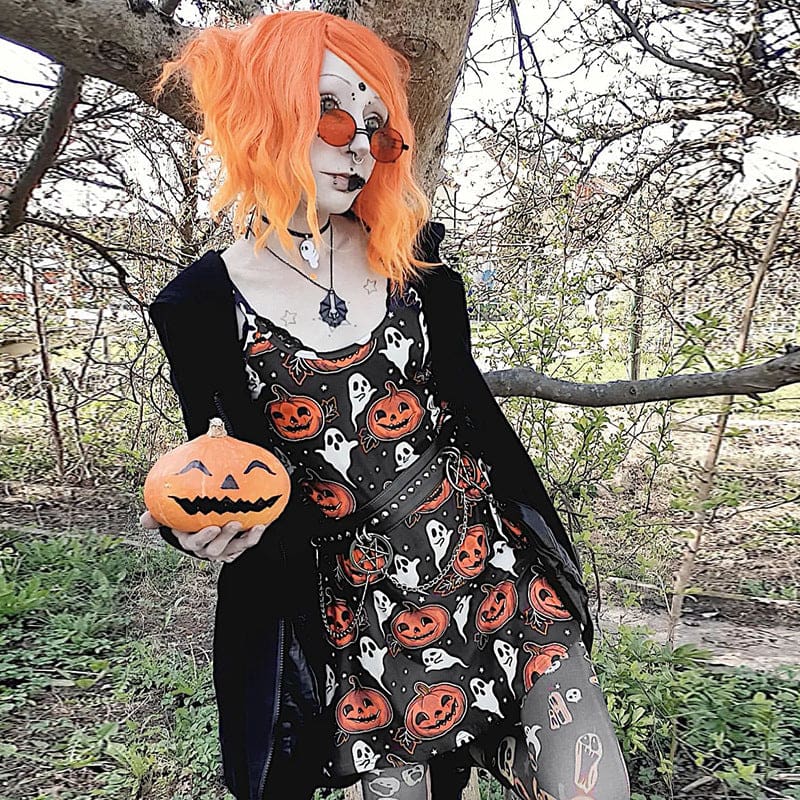 Orange-haired model in orange glasses holds a pumpkin outdoors while wearing the black jack-o-lantern and ghost mini dress.