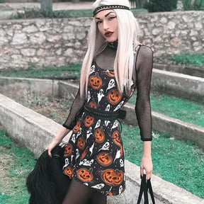 Angled outfit view of the black pumpkin-and-ghost skater dress beside stone steps, styled with black accessories and a sheer underlayer.