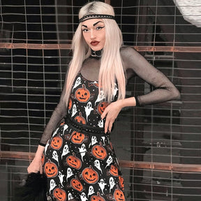 A blonde-haired model poses with a hand at the waist of the black pumpkin-print dress against brick, with a mesh top visible underneath.