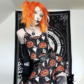 An orange-haired model wears the sleeveless black pumpkin dress against a black-and-white patterned backdrop, with one arm raised beside the thin straps.