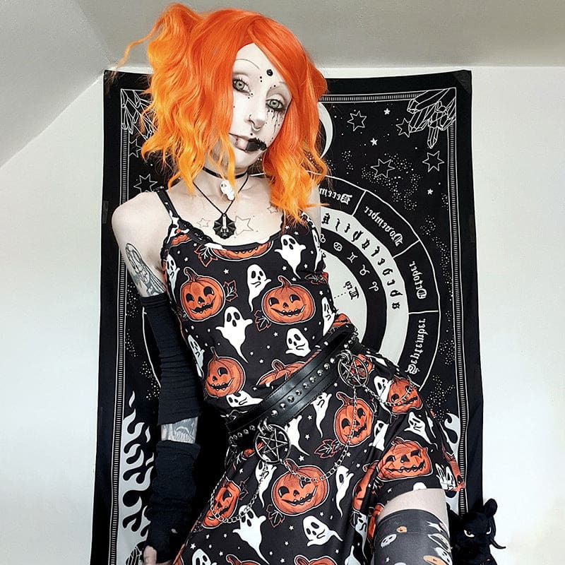 An orange-haired model wears the sleeveless black pumpkin dress against a black-and-white patterned backdrop, with one arm raised beside the thin straps.