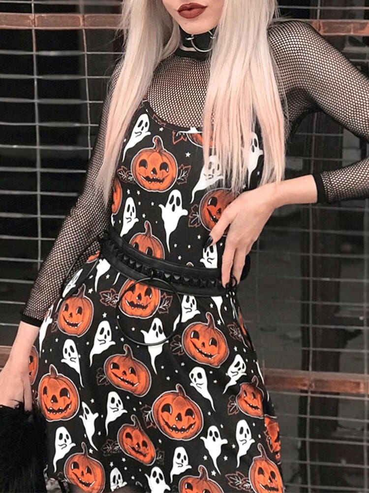 Black pumpkin-and-ghost mini dress styled over a sheer mesh top with a black belt, photographed on a blonde-haired model beside a brick wall.