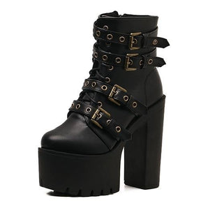 Black buckle boots angled toward the viewer, with brass-tone eyelets and straps crossing the laces.