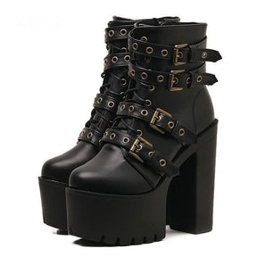 Pair of black punk platform ankle boots with brass-tone buckle straps, front lacing and tall block heels on white.
