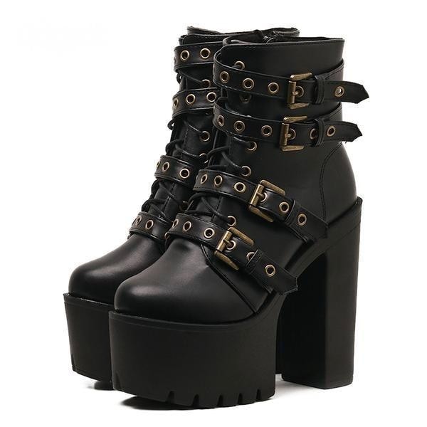 Pair of black punk platform ankle boots with brass-tone buckle straps, front lacing and tall block heels on white.