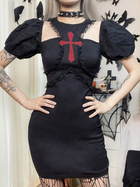 A model poses with both hands at the waist of the black cross mini dress, keeping the puff sleeves, lace under-bust seams and open chest cutouts visible.