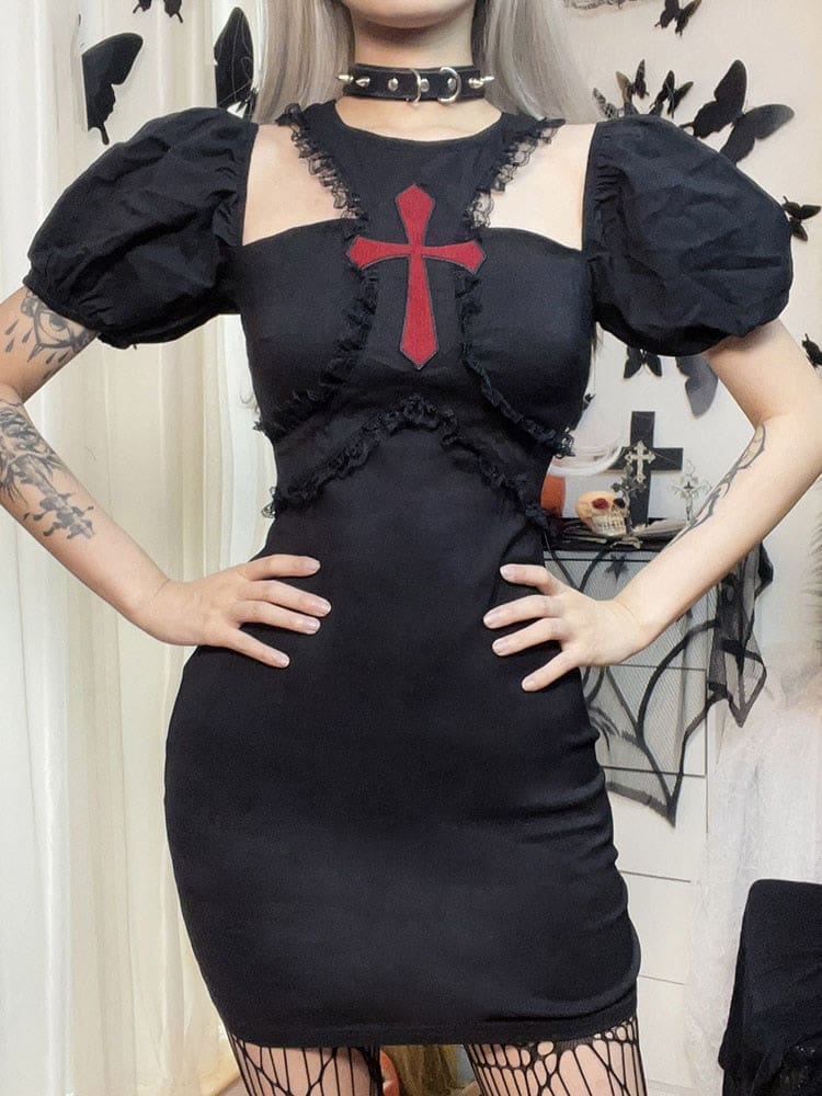 A model poses with both hands at the waist of the black cross mini dress, keeping the puff sleeves, lace under-bust seams and open chest cutouts visible.