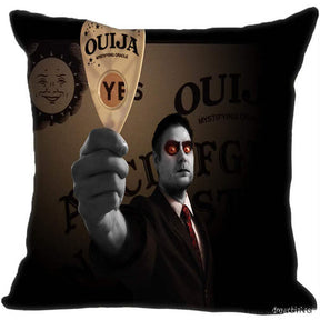 Dark square spirit-board cushion cover featuring an illustrated red-eyed figure holding a printed planchette in front of a brown board.
