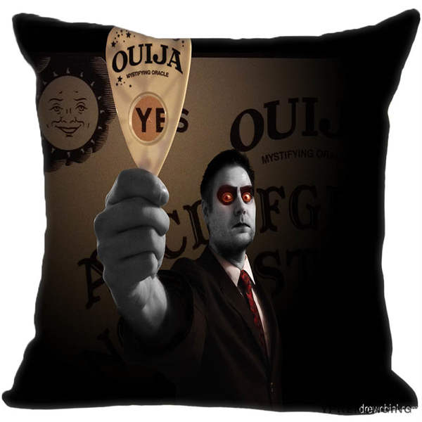 Dark square spirit-board cushion cover featuring an illustrated red-eyed figure holding a printed planchette in front of a brown board.
