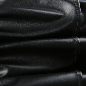 Macro view of the textured black faux leather used in the ruffle skirt, with reflected light across the surface.