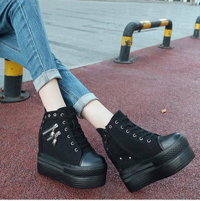 Black skull zipper platform sneakers worn outdoors with cuffed blue jeans beside a red pavement strip.