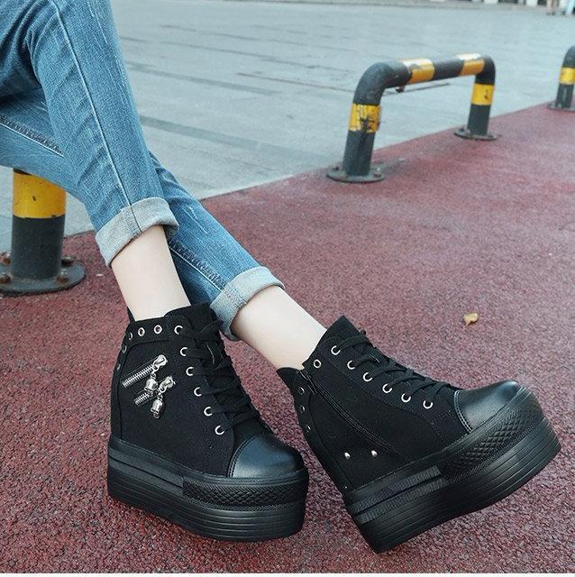 Black skull zipper platform sneakers worn outdoors with cuffed blue jeans beside a red pavement strip.
